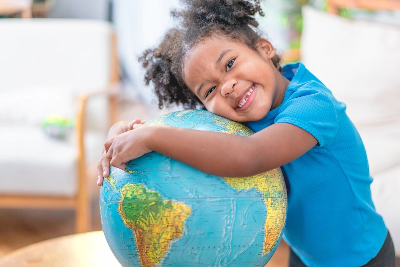 menina sorrindo deitada sobre o globo terrestre