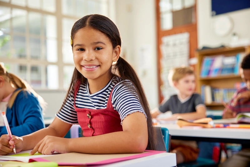 aluna em sala de aula com lapis na mao e sorrindo